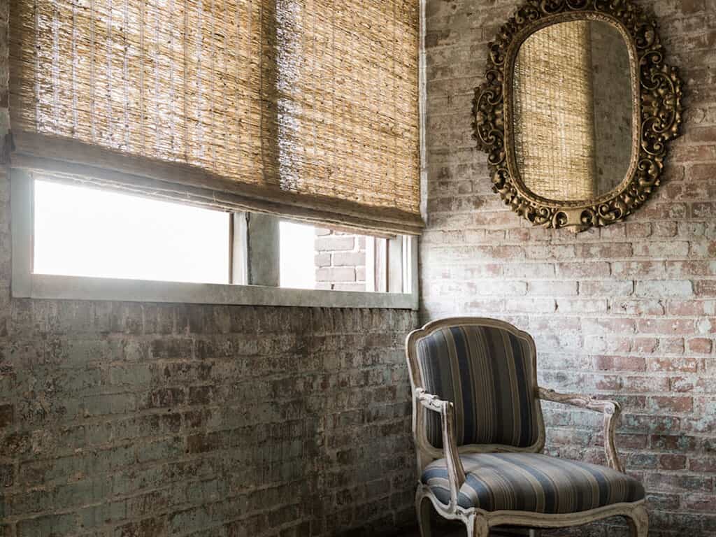 corner of room with brick walls and formal chair with bamboo blinds on window