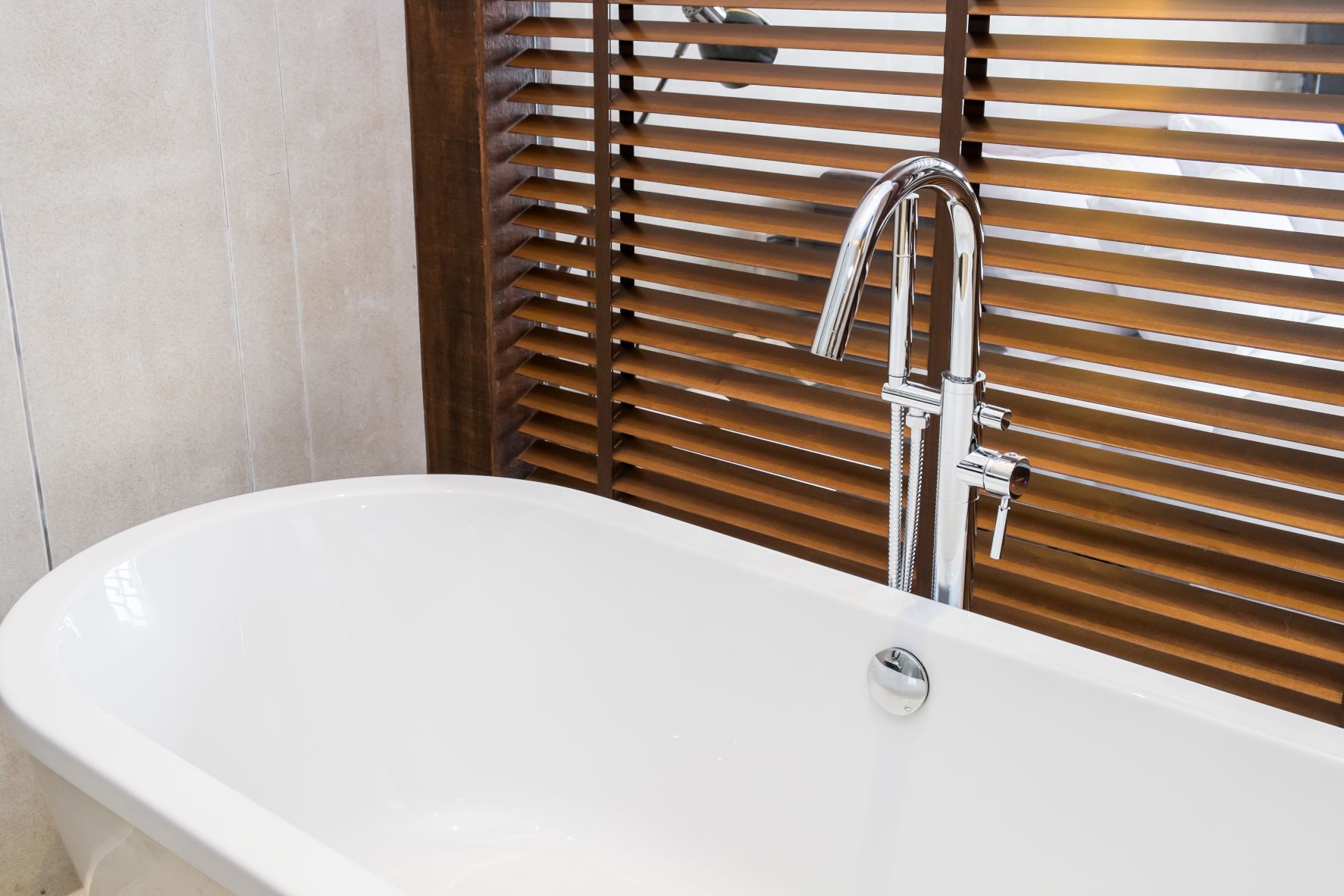 faux wood shutters over a large window by a tub