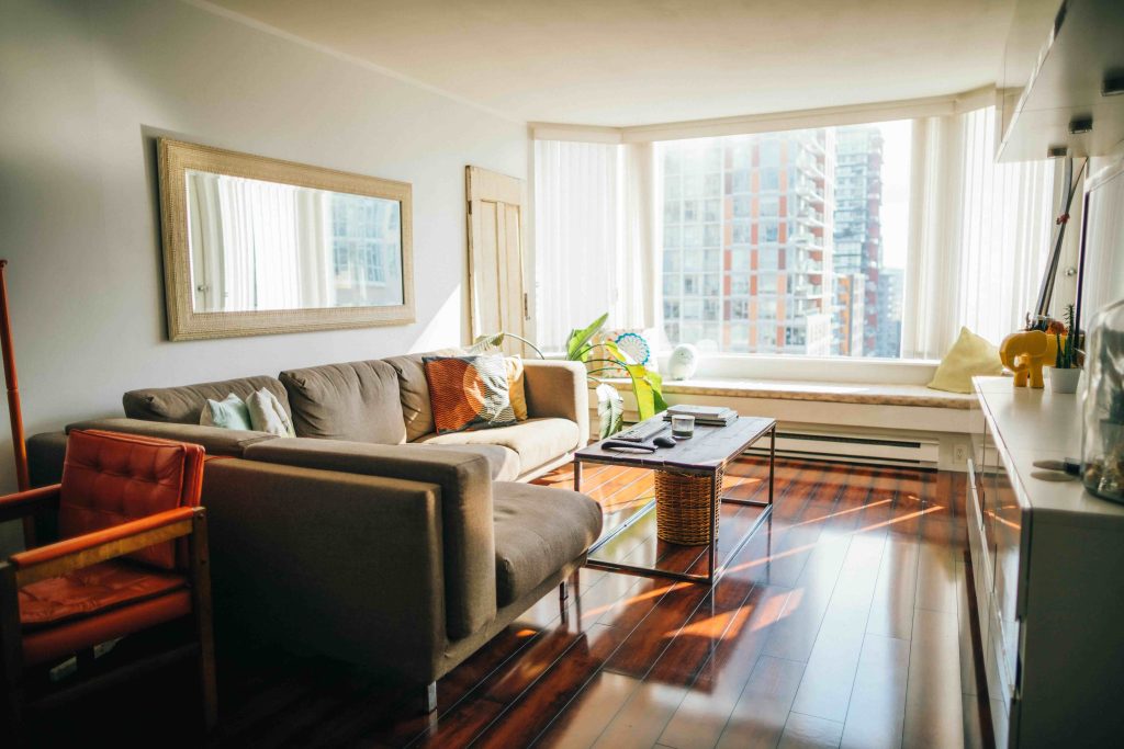 small cozy living room with a mirror on the wall above couch, wood floors and sheer blinds